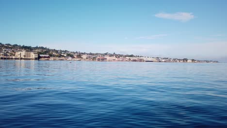 Gimbal-wide-shot-of-Cannery-Row-from-a-moving-boat-on-the-ocean-off-the-coast-of-Monterey,-California