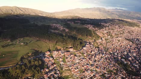 Descending-drone-shot-of-a-city-next-to-a-tree-forrest-in-Cuzco