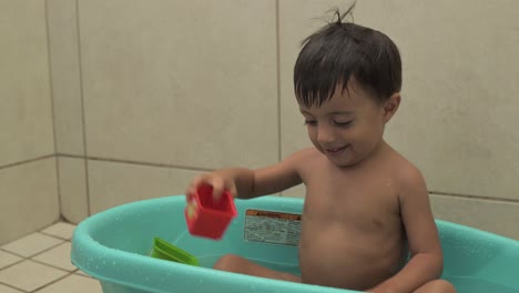 Kleiner-Lateinischer-Junge,-Der-In-Seiner-Blauen-Wanne-Spielt,-Während-Er-Ein-Bad-Mit-Bunten-Spielzeugen-Nimmt,-Die-Wasser-Spritzen