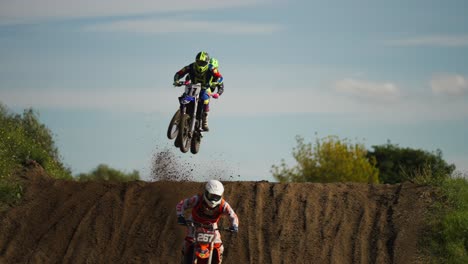 Skilled-motocross-riders-on-dirt-track-jumping-over-hill,-moto-competition,-slow-motion