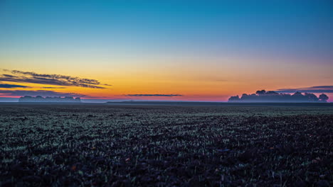 Breitbild-Zeitraffer-Eines-Riesigen-Ackerlandes-Vor-Einem-Orangefarbenen-Sonnenuntergang,-über-Dem-Einige-Dunkle-Wolken-Vorbeiziehen