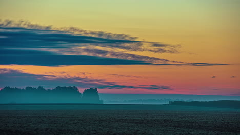 Clouds-flow-across-the-sunrise-sky-on-a-cold-morning-causing-an-inversion-over-the-farmland-fields---time-lapse