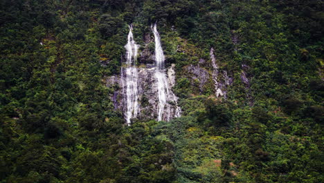 Waterfall-cascading-down-rocky-tall-cliff-in-New-Zealand,-aerial-drone-view