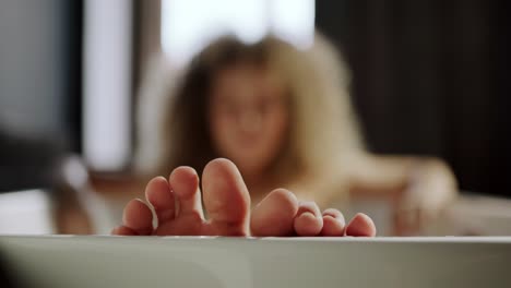 Happy-woman-relaxing-and-enjoying-life-while-taking-a-shower-in-a-tub,-bokeh-close-up-of-toes