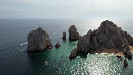 Aerial-view-around-boats-driving-around-the-rocky-arch-of-Cabo-San-Lucas,-Mexico---circling,-drone-shot