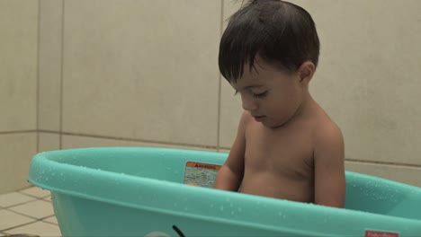 Little-latin-baby-boy-playing-in-his-blue-tub-while-taking-a-bath-with-colorful-toys