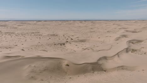 Drone-Flying-Over-Sand-Dune-Landscape,-Blue-Skies-Above-and-Soft-Sandy-Dunes-Below
