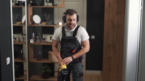 Close-up-of-man-in-uniform-singing-in-headphones-and-cleaning-with-cordless-vacuum-cleaner