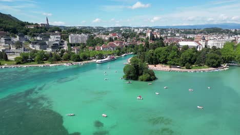 Lake-Annecy,-France---Pedal-Boats,-Turquoise-Light-Blue-Lake-and-Old-Town-Cityscape---Aerial