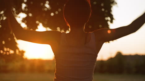 Close-up-over-the-shoulder-of-a-short-haired-woman-doing-jumping-jacks-while-facing-a-beautiful-sunset