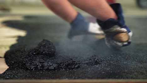 Manual-workers-lay-a-new-asphalt-coating-on-ground-using-hot-bitumen-with-tar-at-construction-site---hands-close-up