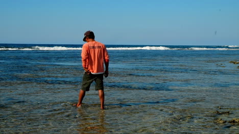 Hombre-Caminando-En-El-Agua-En-Bacnotan-La-Union-Beach,-Isla-Immuki,-Filipinas