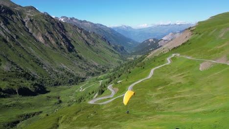Paraglider-fly-above-Col-du-Glandon-Mountain-Pass-in-French-Alps,-Aerial-Truck-Left