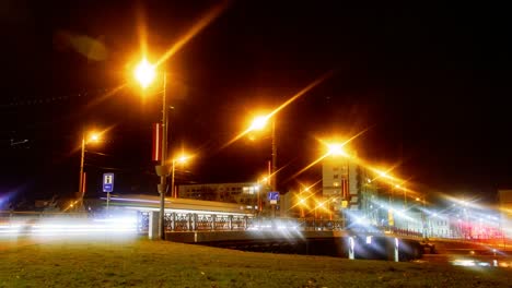 Zeitraffer-Des-Stadtverkehrs-über-Die-Liepaja-Straßenbahnbrücke,-Stadtlandschaft,-Ampelstreifen,-Schnell-Fahrende-Straßenbahnen,-Liepaja-Stadtkanal-Im-Vordergrund,-Im-Nebel-Leuchtende-Lichter-Der-Stadt,-Totale