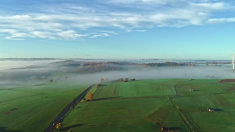 Drone-revealing-vast-and-majestic-landscapes-of-Germany-covered-with-mist-and-wind-turbines-in-the-distance