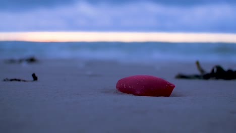 Red-plastic-garbage,-trash-and-waste-litter-on-an-empty-Baltic-sea-white-sand-beach,-environmental-pollution-problem,-overcast-evening-after-sunset,-closeup-shot