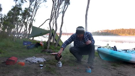 A-bush-man-pours-a-coffee-with-his-billy-on-a-kayak-camp-on-an-Australian-lake