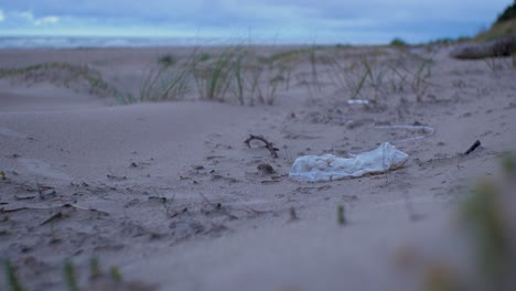 Plastic-bag,-trash-and-waste-litter-on-an-empty-Baltic-sea-white-sand-beach,-environmental-pollution-problem,-overcast-evening,-distant-medium-shot