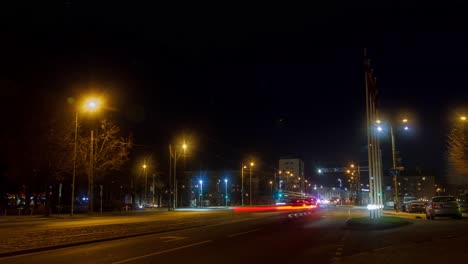 Timelapse-of-city-rush-hour-traffic-on-the-street-of-Liepaja,-traffic-light-streaks,-tram-rails-with-fast-moving-trams,-pedestrians-waiting-for-the-public-transport,-wide-shot