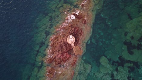 Top-down-aerial-view-of-small-lonely-lighthouse-on-offshore-rocks,-zoom-out