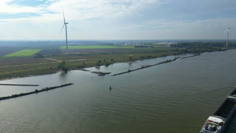Luftaufnahme-Der-Riesigen-Windkraftanlage-Mit-Dolly-Direkt-über-Der-Oude-Maas-Mit-Vorbeifahrendem-Lastkahn