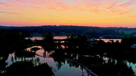 Sunrise-glow-above-Amatciems-lake-and-resort-in-Latvia,-aerial-ascend-view