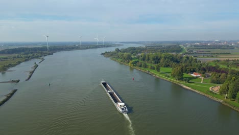 Luftaufnahme-über-Den-Lastkahn,-Der-Entlang-Der-Oude-Maas-Fährt,-Mit-Einer-Reihe-Von-Windkraftanlagen-In-Der-Ferne