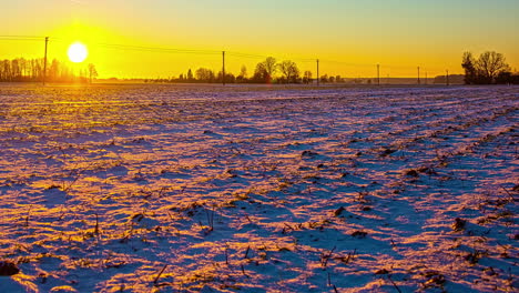 Bright-sun-setting-down-behind-snow-covered-agriculture-fields,-fusion-time-lapse