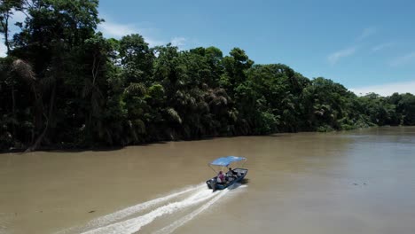 Two-men-in-motorboat-with-roof-cruising-fast-on-dirty-jungle-river