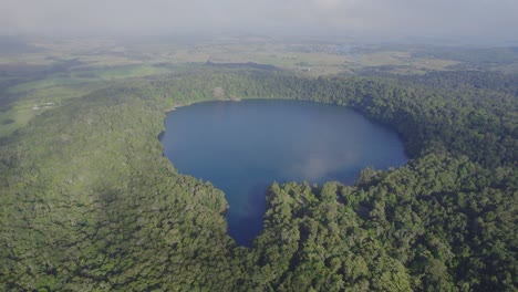 Lake-Eacham-Surrounded-With-Lush-Rainforest-And-Vegetation-In-Atherton-Tableland,-Queensland,-Australia---aerial-shot