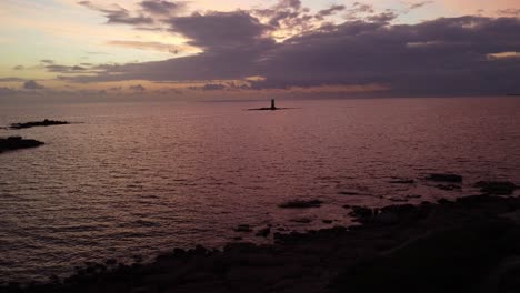 Static-shot-of-offshore-rocks-with-flashing-Lighthouse-in-middle-of-sea-at-dusk
