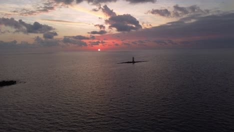 Incredible-aerial-view-of-sun-setting-below-sea-horizon-with-offshore-lighthouse