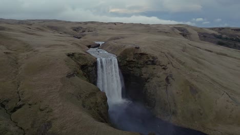 A-drone-flies-forward,-tilting-over-the-waterfall-of-Skógafoss-in-Iceland