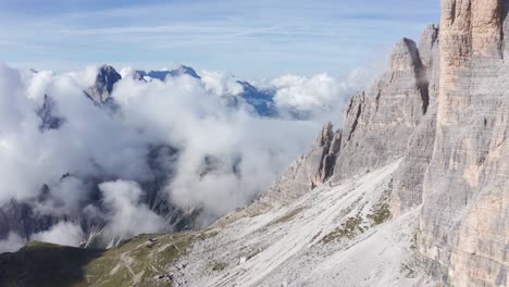 Aerial-view-of-steep-rocky-wall-of-Tre-Cime-and-low-clouds-in-the-Dolomites,-Italy