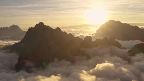 Stunning-golden-sunrise-clouds-surrounding-South-Tyrol-Tre-Cime-Dolomites-mountains-aerial-view-orbiting-ethereal-landscape
