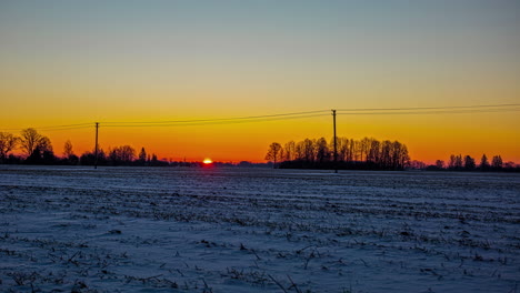 At-sunrise,-the-fiery-sun-rises-above-the-horizon-and-illuminates-the-snowy-European-countryside---time-lapse