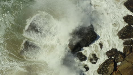 Slowmotion-aerial-shot-above-a-rock-with-waves-crashing-over
