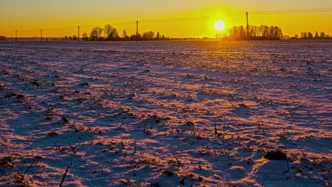 Sunrise-over-a-plowed-farmland-field-in-the-European-countryside-with-the-golden-rays-of-the-sun-reflecting-off-the-snow---time-lapse