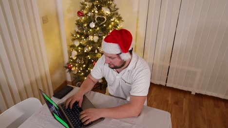 caucasian-entrepreneur-working-online-remotely-during-the-Christmas-holiday-in-his-home-office-house-with-Xmas-tree-decorated-and-lit-up,-top-high-angle-view