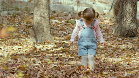 Young-Asian-girl-stares-at-feet-buried-in-autumn-leaves-while-playing-in-park