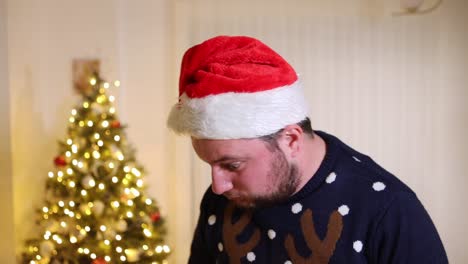 Hombre-Caucásico-Solitario-Con-Sombrero-De-Santa-Lleno-De-Rabia-Y-Enojo-Durante-Las-Vacaciones-De-Navidad-En-Casa-Con-Un-árbol-De-Navidad-Decorado-En-El-Fondo