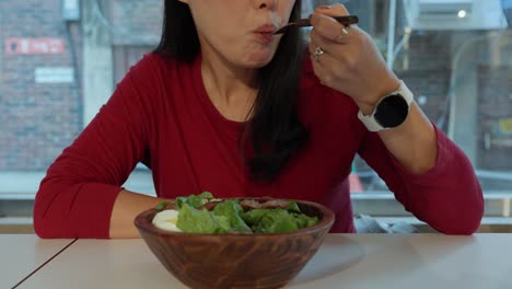 Korean-woman-takes-bite-of-salad-from-wooden-bowl-with-fork