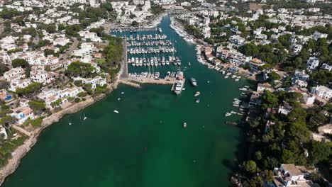 Aerial-view-of-drone-flying-to-cala-d'Or-harbor-and-beach-of-Mallorca-filled-with-boats-and-yachts-during-summer