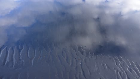 Top-down-shot-of-mud-waves-in-black-sand-of-Icelandic-beach-during-cloudy-day
