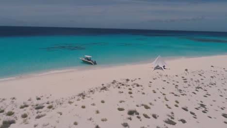 White-luxury-beach-camp-on-paradise-island,-aerial-view-turn-around-coast-with-boat-moored