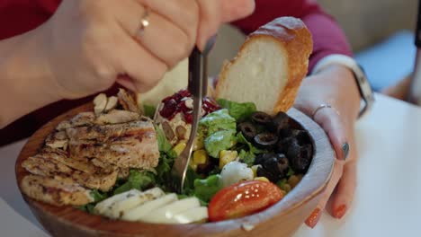 Woman-begins-eating-fresh-grilled-chicken-salad-from-wooden-bowl