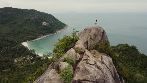 Woman-is-standing-on-top-of-a-cliff,-looking-over-and-enjoying-the-majestic-view-of-the-sea