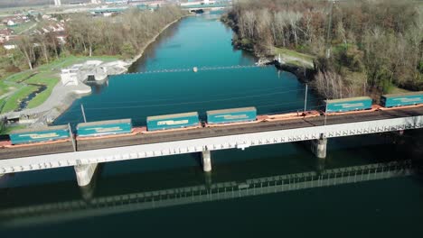 A-long-freight-train-carrying-shipping-container-driving-over-a-beautiful-river-in-Austria-via-a-railway-bridge