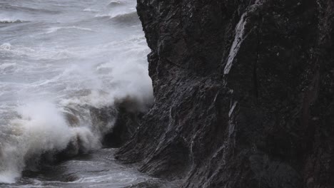 Slow-motion,-stormy-ocean-waves-crash-against-rocky-coastal-cliff