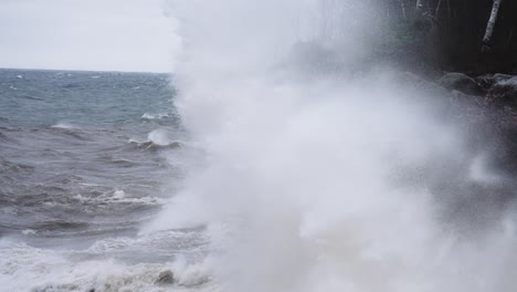 Ocean-wave-crash-against-granite-coastal-cliff-in-slow-motion-on-a-gloomy-day